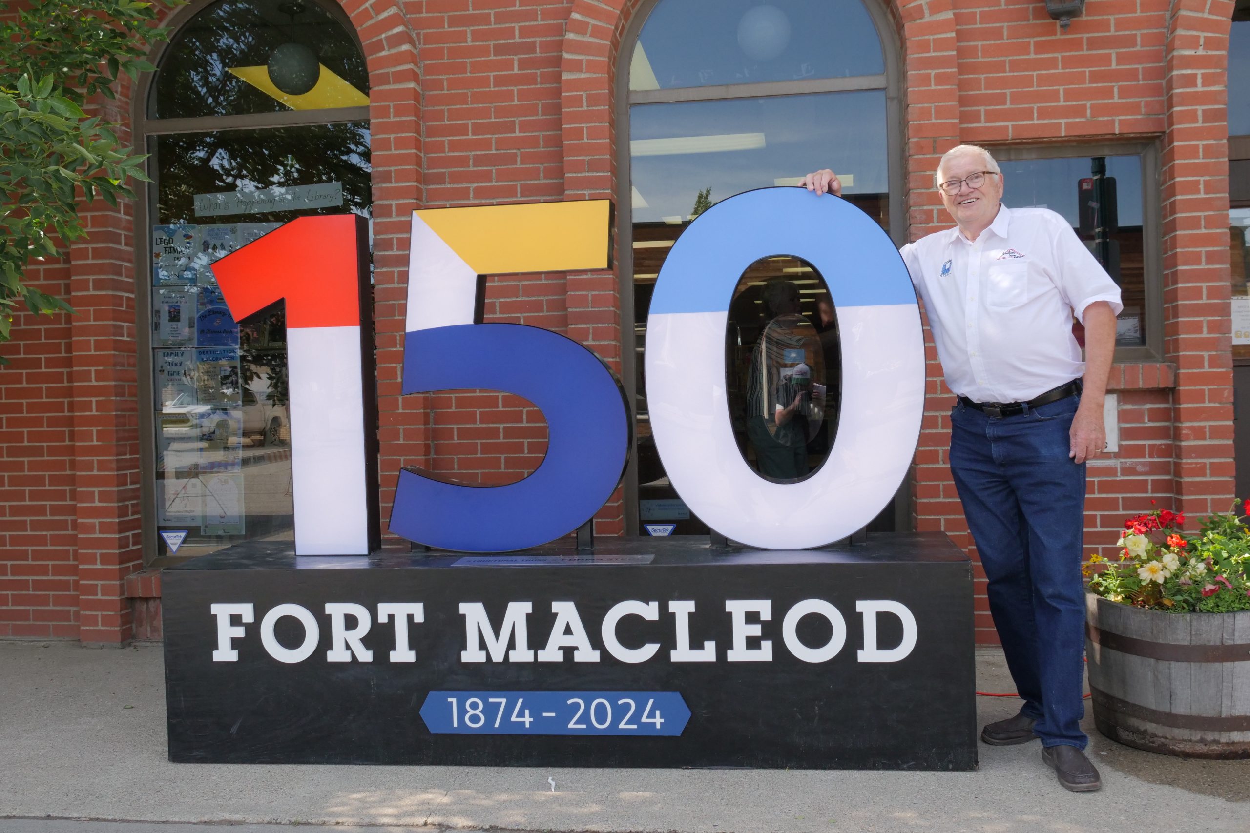 Community Project: Founder Frans Feyter stands with Fort Macleod 150 Birthday Sign